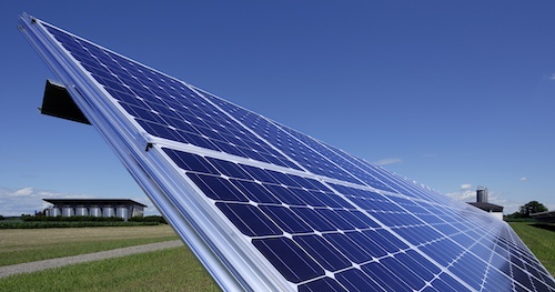Schräg geneigte Solaranlage mit Solarzellenpaneelen im Feld unter blauem Himmel.