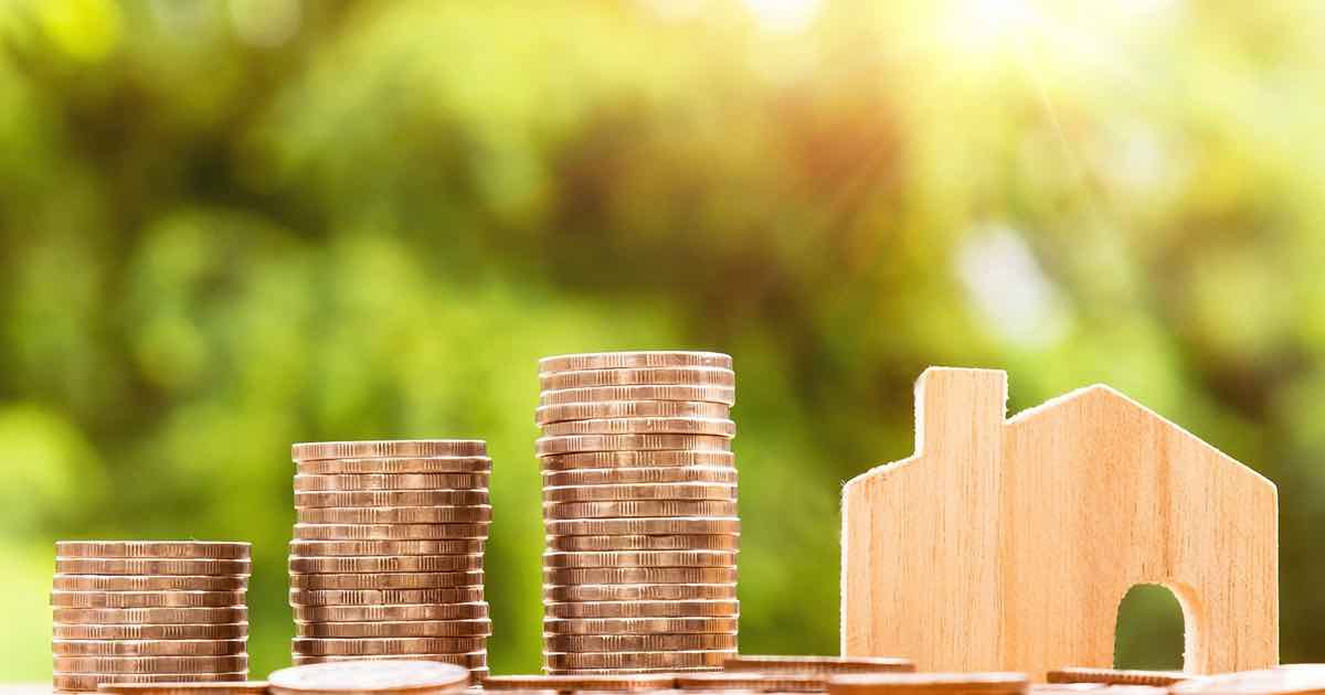 Stapel kupferner Münzen unterschiedlicher Höhe neben einem kleinen Holzhäuschen; unscharfer grüner Gartenhintergrund.