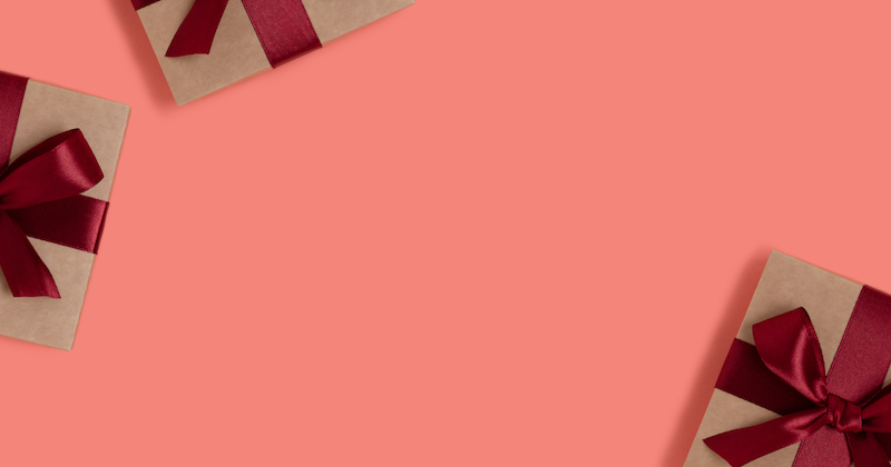 Drei Geschenkboxen mit roten Schleifen auf rosafarbenem Hintergrund