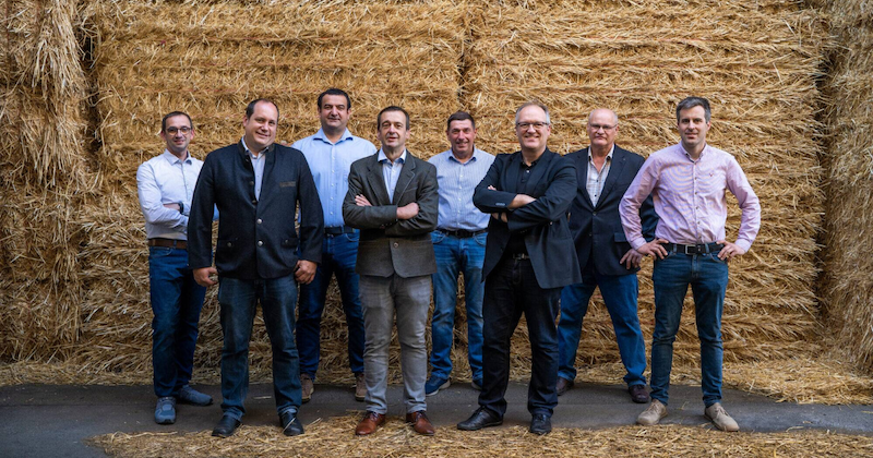 Gruppe von acht Personen in Business- und Freizeitkleidung posiert vor Strohballen.