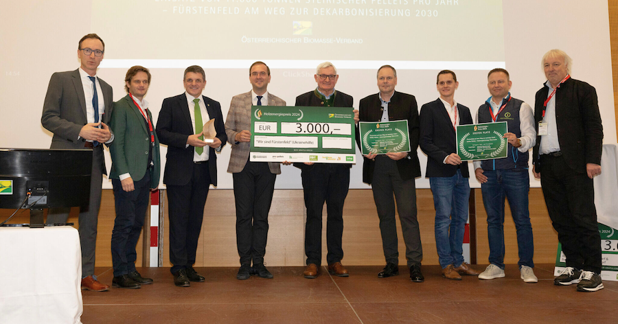 Gruppe von Personen auf einer Bühne hält einen großen Scheck und Zertifikate während einer Preisverleihung.