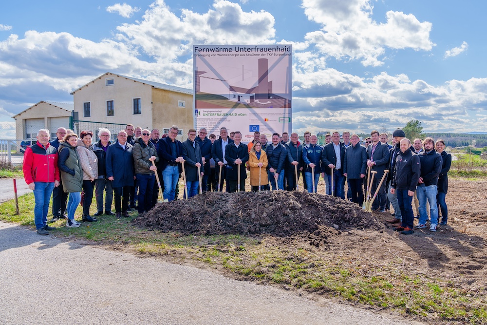 Gruppe von Personen beim Spatenstich vor Gebäuden und dem Banner Fernwärme Unterfrauenhaid; Erdhaufen im Vordergrund.