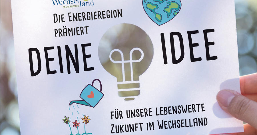 Von einer Person gehaltenes Plakat mit Glühbirne, Gießkanne und Blumen; Text: Die Energieregion prämert deine Idee – Zukunft im Wechselland