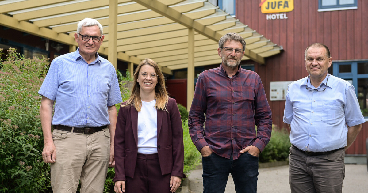 Vier Personen in Business-Casual vor dem JUFA Hotel, posieren freundlich draußen.
