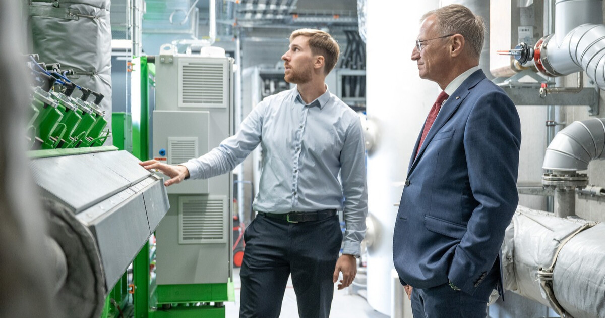 Zwei Personen einer Industrieanlage stehen vor einer großen Bedienkonsole; eine Person bedient das Panel, die andere beobachtet.