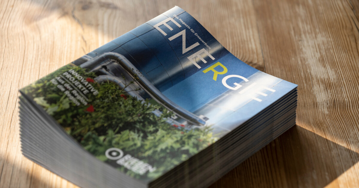 Stapel Zeitschriften auf Holztisch; Titelseite mit blauem Cover und dem Schriftzug ENERG, im Vordergrund grüne Pflanzen.