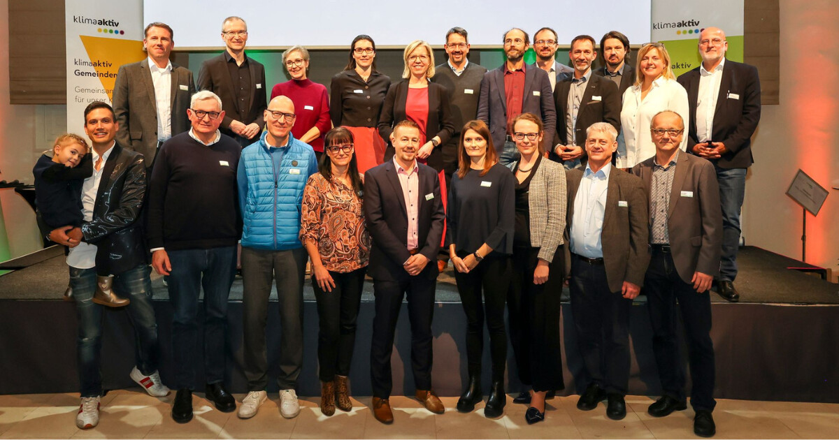 Gruppe von etwa 20 Personen posiert gemeinsam auf einer Bühne bei einer klimaaktiv-Veranstaltung, alle tragen Namensschilder.