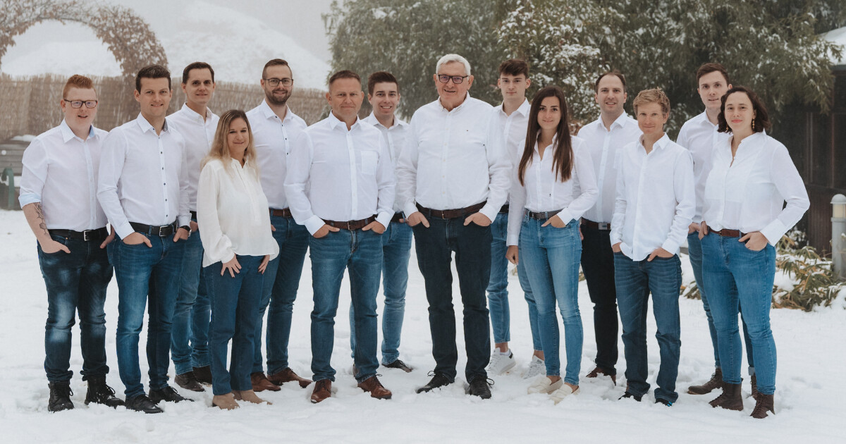 Gruppe von Personen in weißen Hemden und Jeans steht im Schnee im Freien, wirkt freundlich und posiert zusammen.