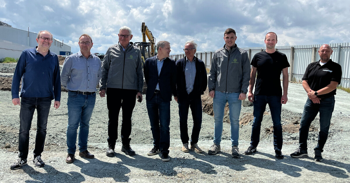Gruppe von Fachleuten steht auf einer Baustelle, im Hintergrund ein Bagger sichtbar.