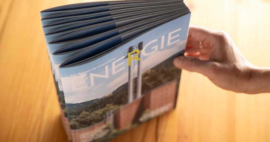 Person blättert durch das Magazin für erneuerbare ENERGIE; das Cover zeigt eine Landschaft mit einem Holzheizwerk