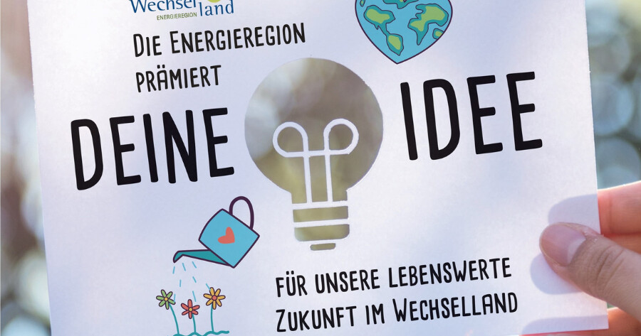 Von einer Person gehaltenes Plakat mit Glühbirne, Gießkanne und Blumen; Text: Die Energieregion prämert deine Idee – Zukunft im Wechselland