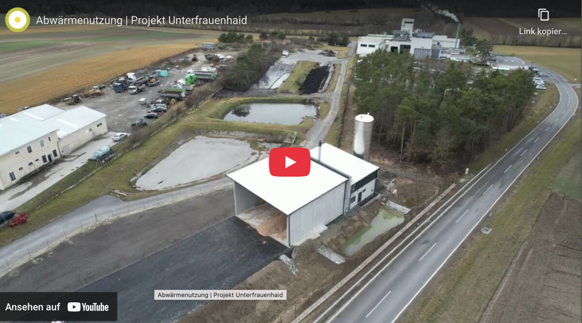 Luftbild einer Abwärmenutzungsanlage mit Gebäuden, Tanks, Becken, Straßen und umgebendem Wald.