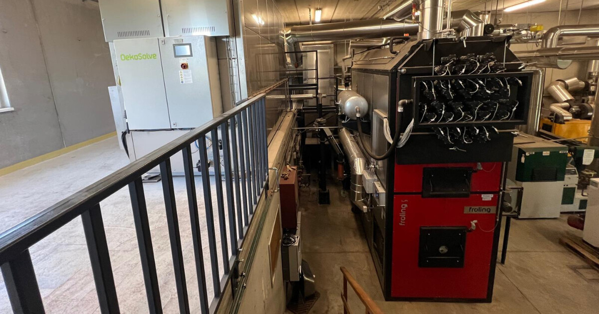 Industrie-Maschinenraum: roter Froling-Kessel mit zahlreichen Rohren, Bedienfelder und Geländer im Vordergrund.