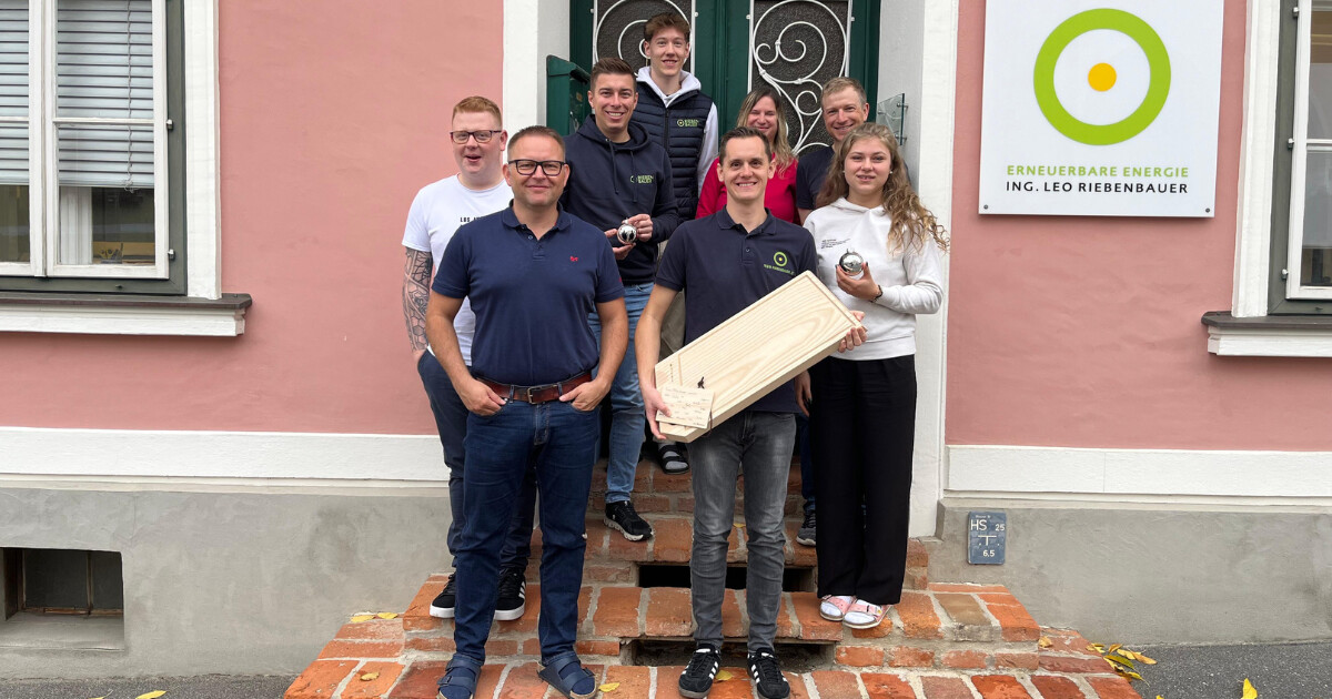 Gruppe von Mitarbeitenden posiert auf roten Ziegelstufen vor einem pinken Gebäude mit Logo Erneuerbare Energie.