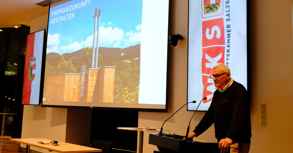 Person am Rednerpult vor Großbildschirm mit dem Titel Energiezukunft gestalten; Banner links und rechts im Veranstaltungsraum.