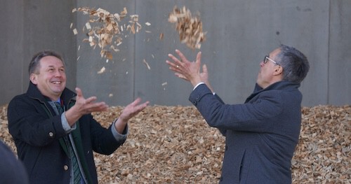 Zwei Personen werfen Hackschnitzel in die Luft vor einer grauen Wand.