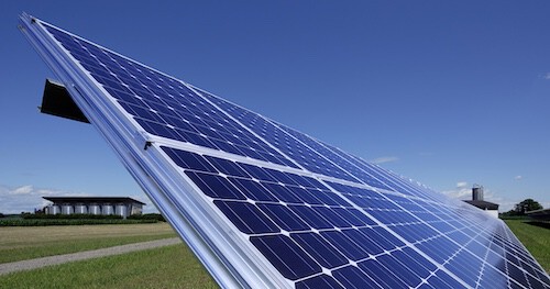 Schräg geneigte Solaranlage mit Solarzellenpaneelen im Feld unter blauem Himmel.