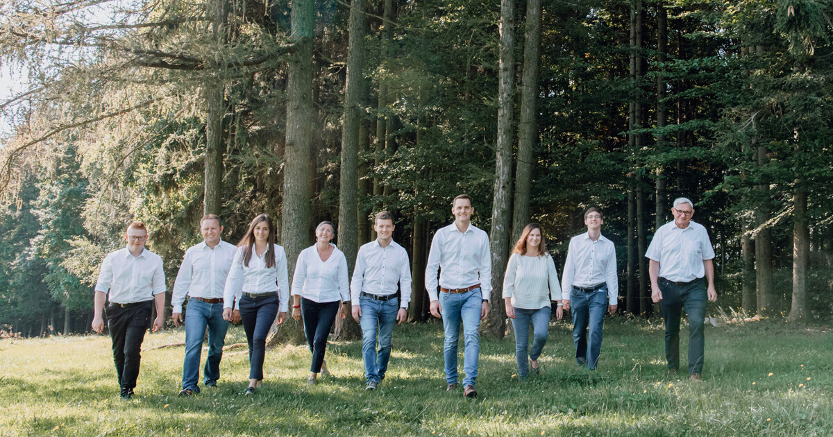 Gruppe von Personen in weißen Oberteilen und Jeans geht durch einen Wald.