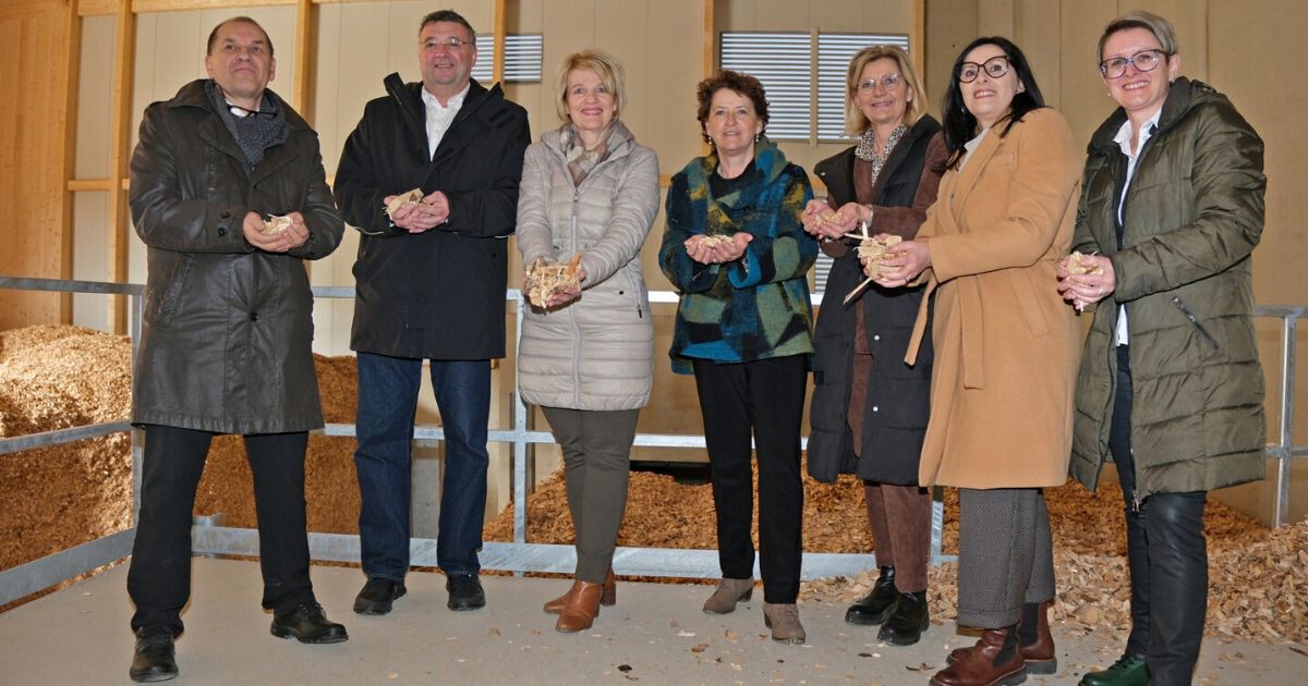 Acht Personen in Winterjacken stehen in einer Holzwerkstatt, halten Holzstücke und Holzspäne, schauen in die Kamera.