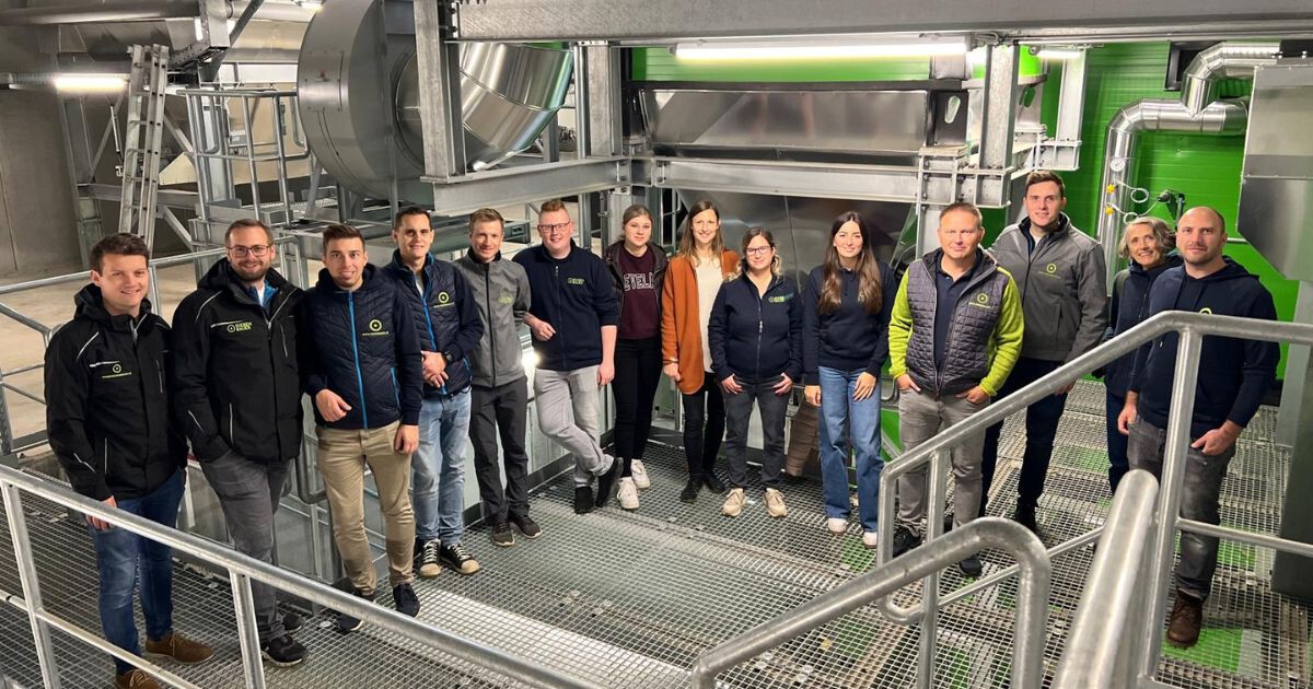 Gruppe von Mitarbeitenden in einer Produktionsanlage vor einer großen Industriemaschine.