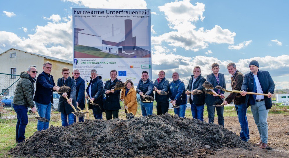 Gruppe von Personen beim Spatenstich für Fernwärme Unterfrauenhaid, mit Schaufeln, vor Plakat des Projekts.