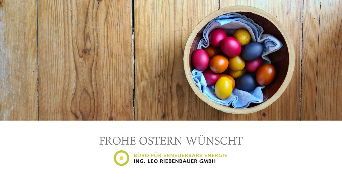 Runder Holzkorb mit bunten Ostereiern, ausgelegt mit blauem Tuch, auf Holztisch.