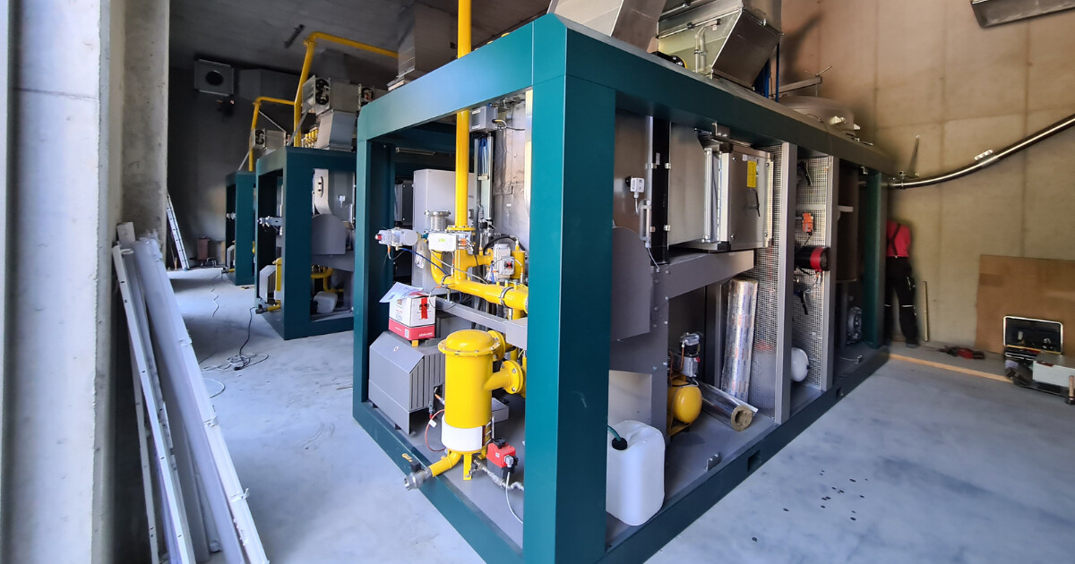 Große industrielle Anlage mit gelben Rohrleitungen, grünem Stahlrahmen und Motoren; eine Person arbeitet an der Maschine.