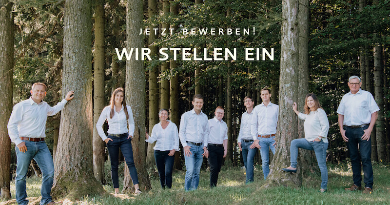 Gruppe von Mitarbeitenden steht im Wald auf Gras; Text 'JETZT BEWERBEN! WIR STELLEN EIN' sichtbar