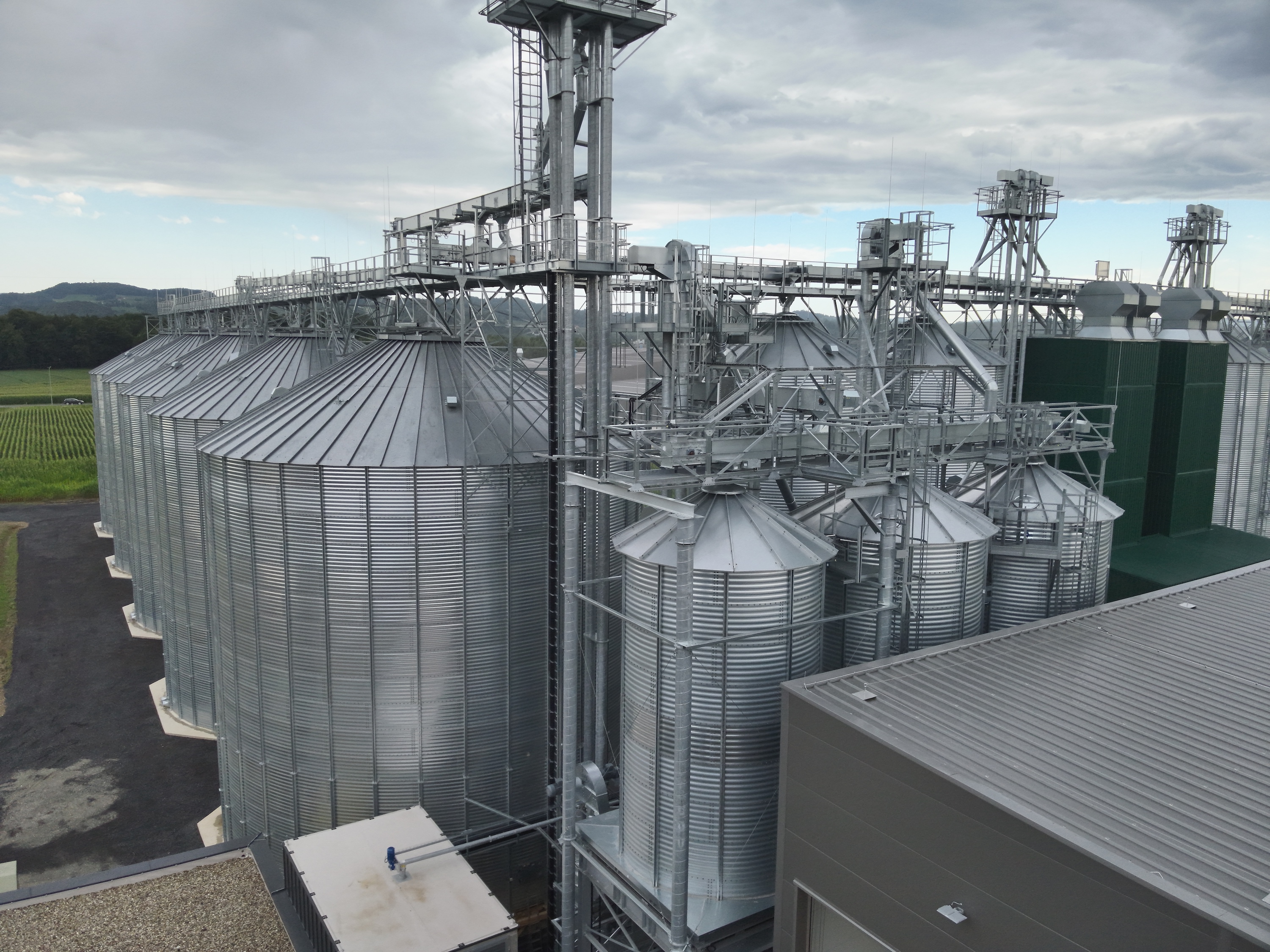 Mehrere große silberne Metall-Silos mit Fördertechnik und Stahlgerüsten auf einer Getreidelageranlage.