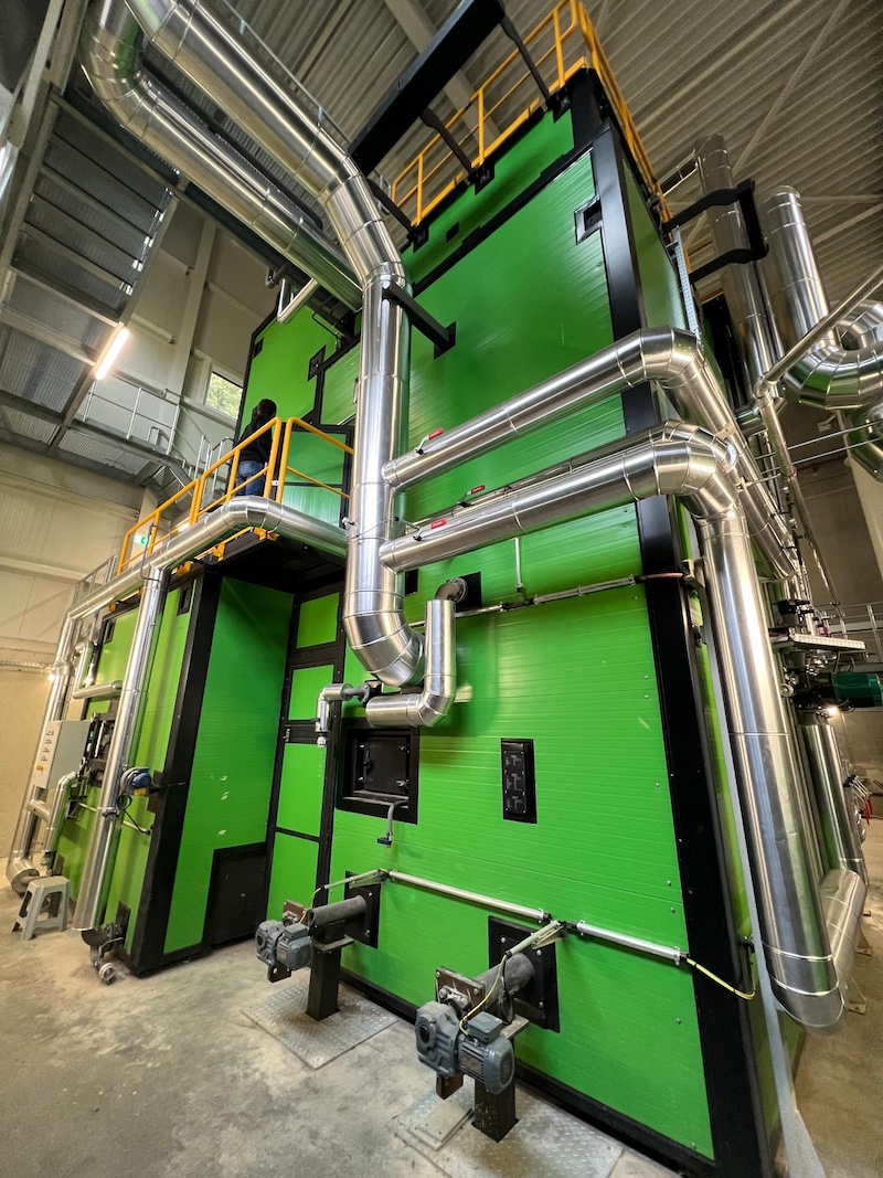 Große grüne industrielle Anlage mit silbernen Rohrleitungen und Geländern; eine Person steht auf dem oberen Gang.