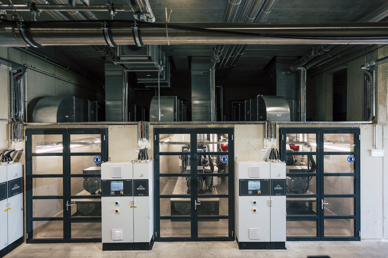 Industrieanlage im Innenraum mit drei Glas-Schiebetüren, Steuer- und Verteilerschränken, Kabelkanälen und Lüftungsrohren.