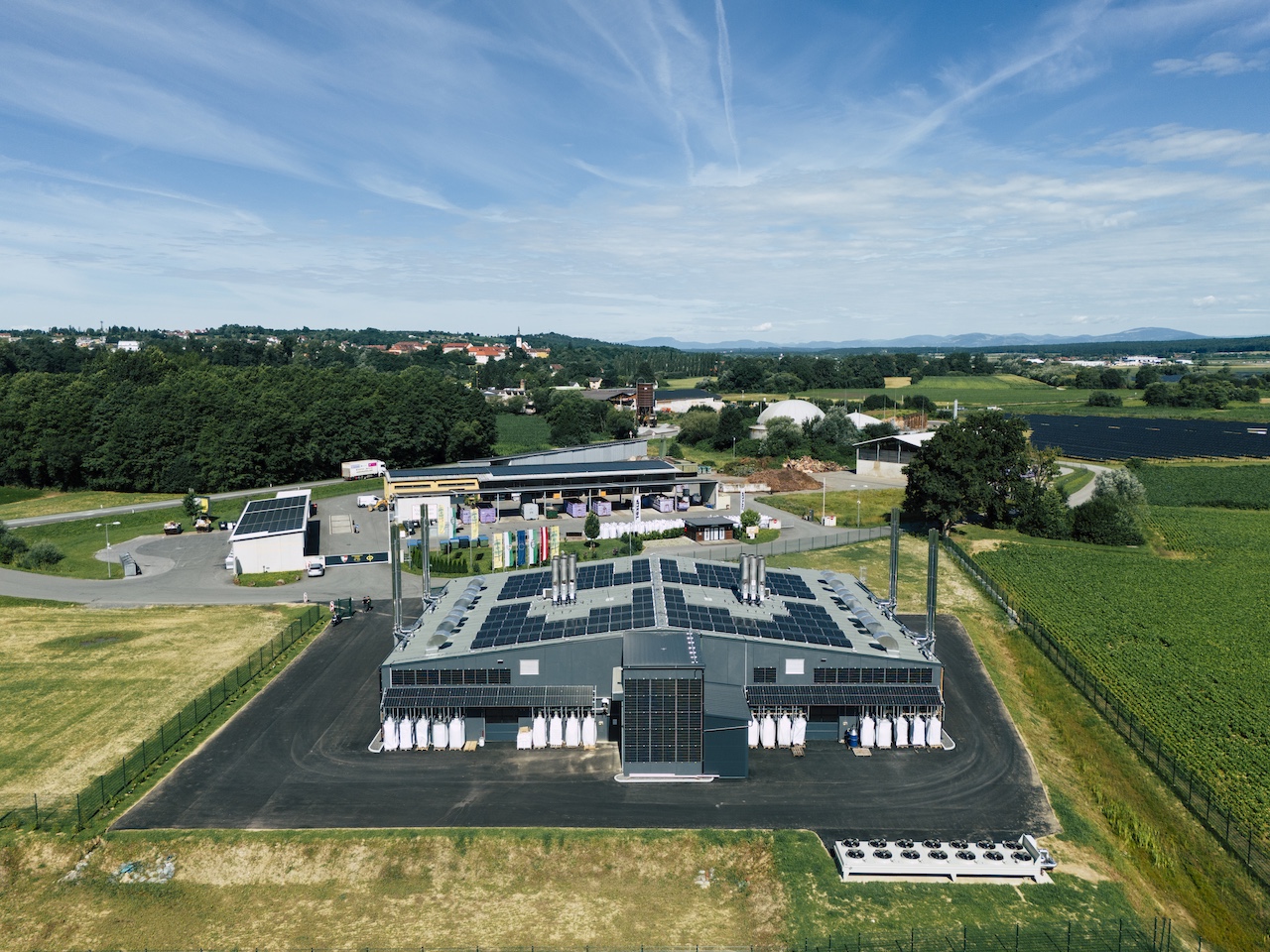 Luftaufnahme einer Industrieanlage mit Dachsolaranlage, umgeben von Feldern, Bäumen und ländlicher Landschaft.