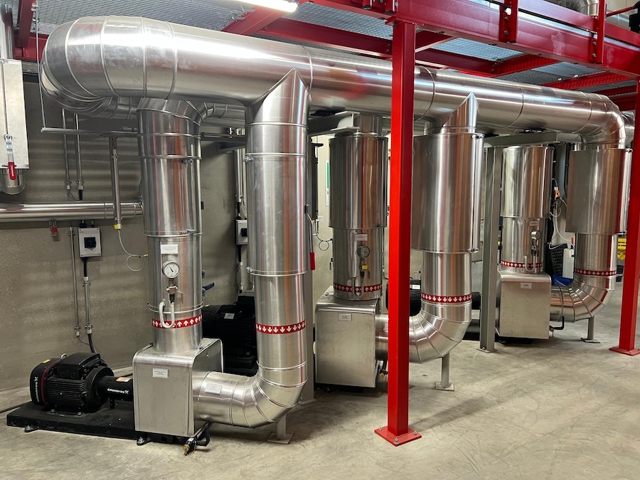 Industrielle Edelstahl-Rohrleitungen, Pumpen und Messgeräte; roter Stahlrahmen im Maschinenraum.