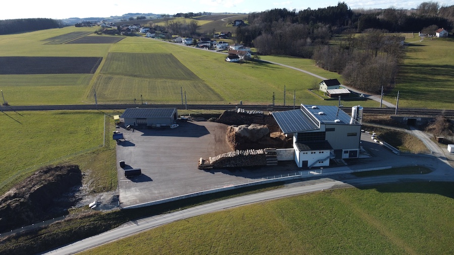 Luftaufnahme einer Industrieanlage mit Erdmassen, Parkflächen und umliegenden Feldern; Straße verläuft am Gelände entlang.