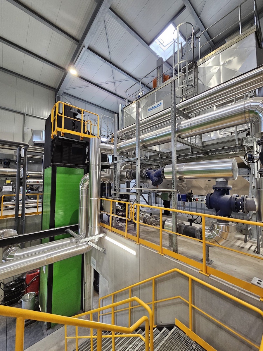 Industrielle Anlage mit Edelstahlrohren, Geländern, Plattformen und Leitungen; grüne Maschine im Maschinenraum.