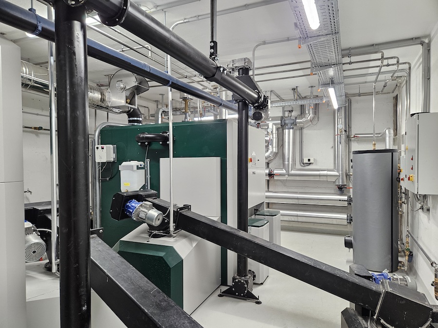Industrieller Technikraum mit Rohren, Leitungen, Pumpen und einer großen grünen Maschine