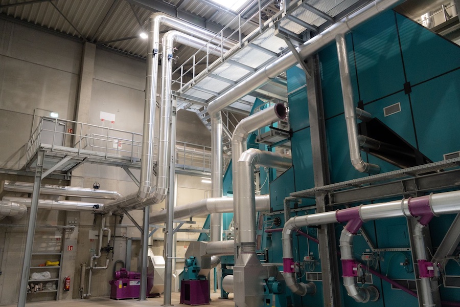 Industrieanlage mit silbernen Rohrleitungen, Turbinen und türkisfarbenen Gehäusen; komplexe Rohrführung in einer Fabrikhalle.