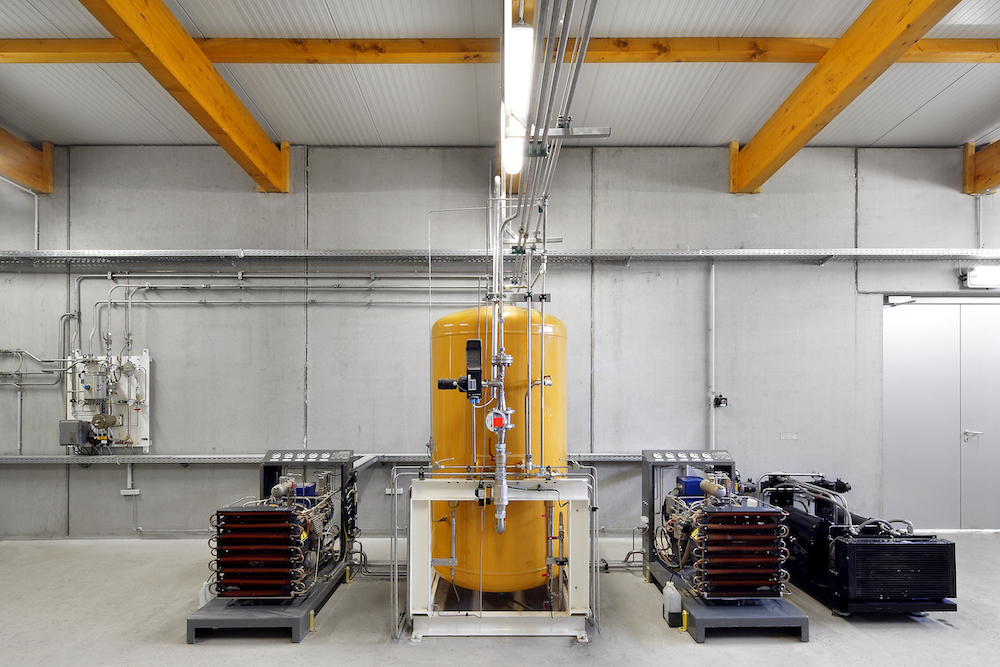 Industrielle Anlage mit zentralem gelben Druckbehälter, Rohrleitungen, Pumpen und Steuereinheiten in einer Werkshalle.