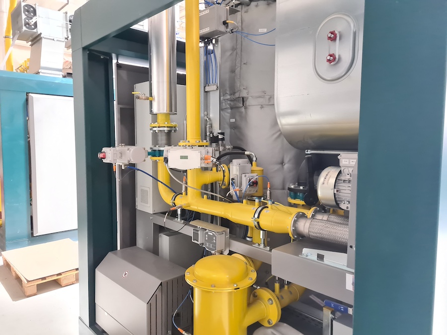 Industrielle Anlage mit gelben Rohrleitungen, Motoren, Pumpen und Steuergeräten in einem Maschinenrahmen.