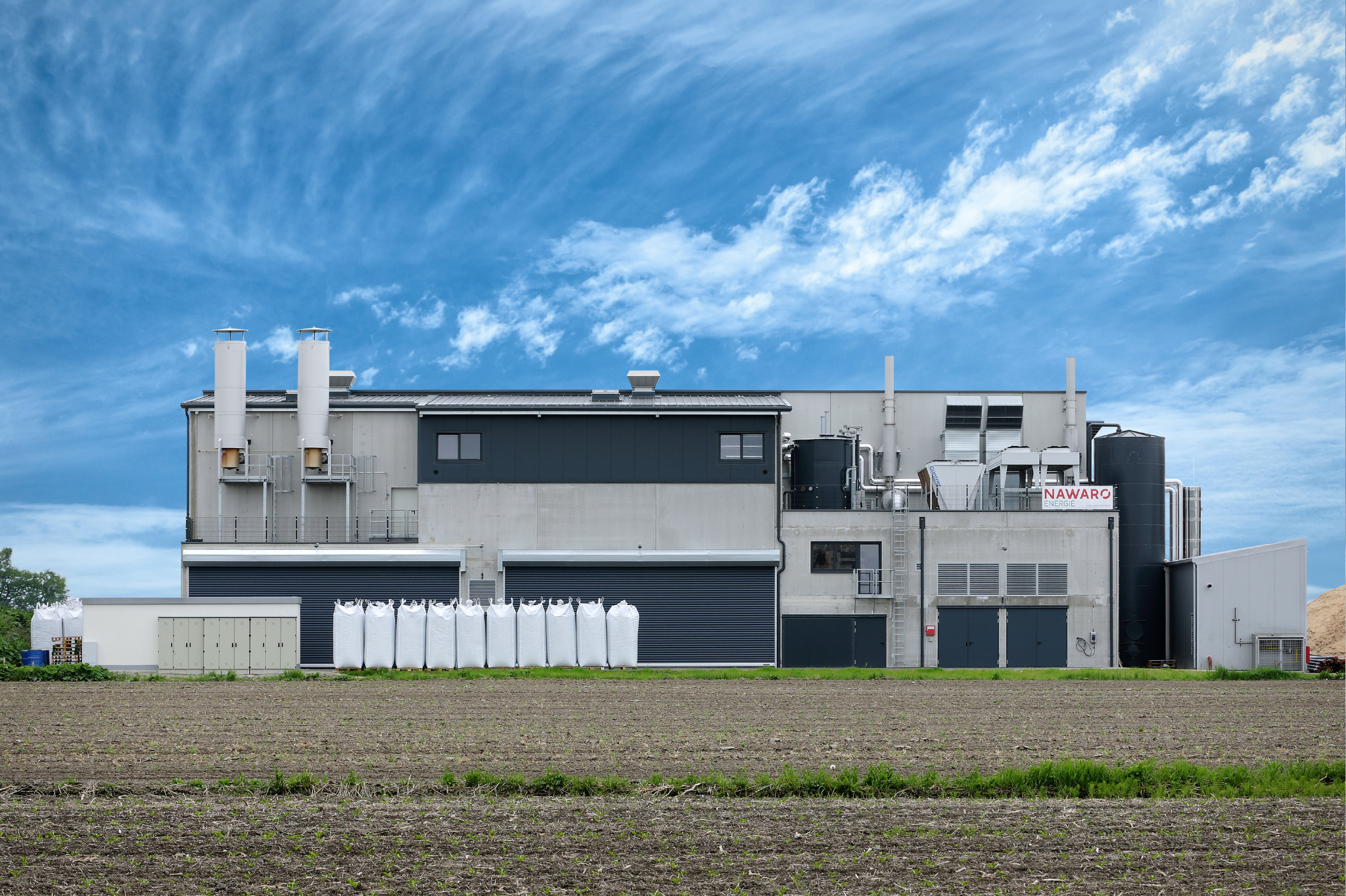 Industrieanlage mit Silos und Tanks vor Ackerland und blauem Himmel