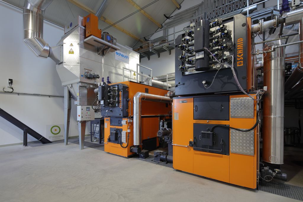 Große industrielle Maschinenanlage in einer Produktionshalle mit orange und grauen Bauteilen, Rohrleitungen und Steuerungselementen.