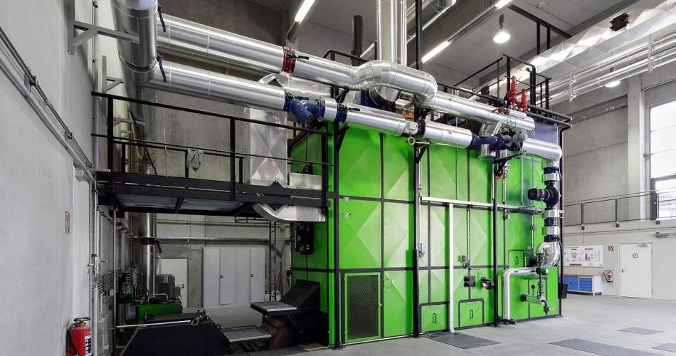 Industrielle Anlage mit großen grünen Schaltschränken, zahlreichen Edelstahlrohren und Metallkonstruktionen in einer Werkhalle.