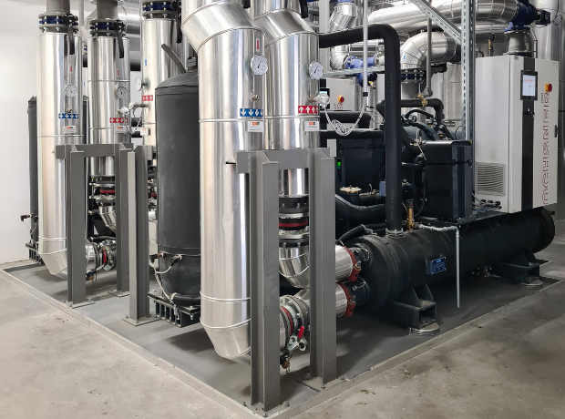 Industrielle Anlage aus Edelstahlrohren, Ventilen, Messgeräten und Pumpen in einem Technikraum.