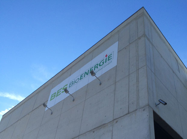 Betongebäude mit BES BIOENERGIE Schild und grünem Logo vor blauem Himmel.