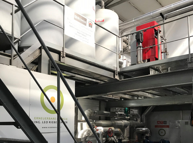 Industrieller Maschinenraum mit Rohren, Leitern und Stahlstrukturen; Schild für erneuerbare Energie sichtbar.