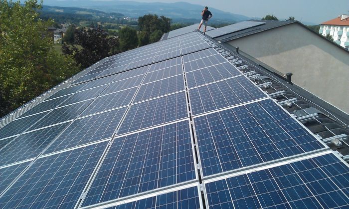 Großes Dach mit vielen blauen Solarzellen; eine Person steht am Rand und blickt über eine hügelige Landschaft.