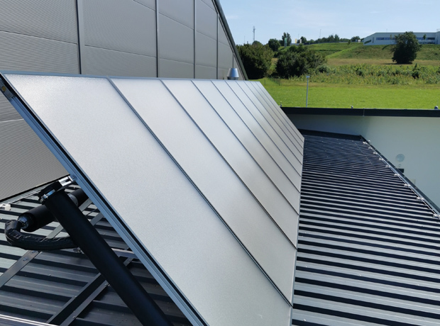 Solarmodule auf einem schrägen Metalldach, silbrige Paneele, PV-Anlage, grüne Landschaft im Hintergrund.