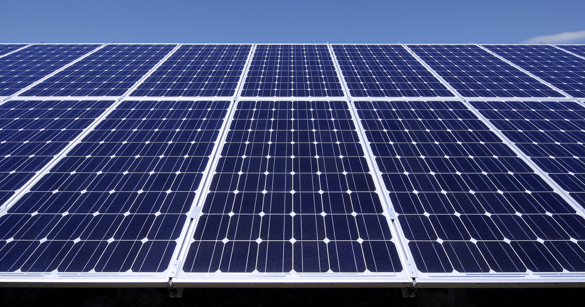 Dichte Reihe blauer Solarmodule in einer großen Solarstromanlage, klarer blauer Himmel im Hintergrund.